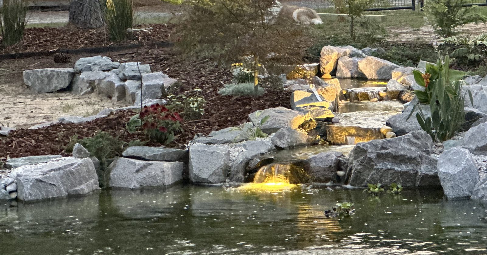 Lit waterfall spilling into a pond at dusk